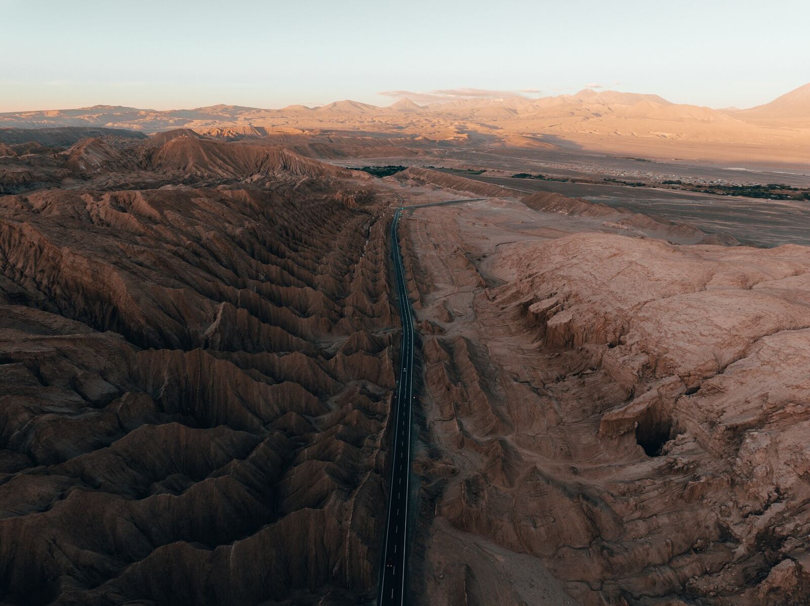 Desert Highway | Love Hurtz A highway cuts through a deeply eroded desert landscape at sunset, evoking feelings of isolation and the journey through.