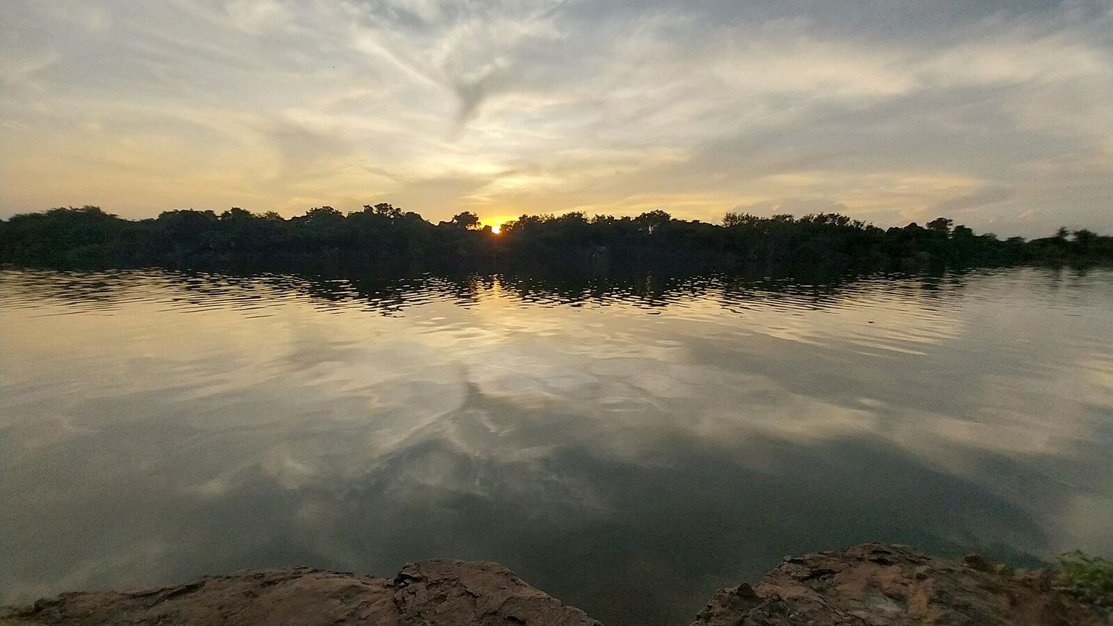 Godavari River Landscape | Love Hurtz A tranquil river reflects the cloudy sky and distant trees at sunset.