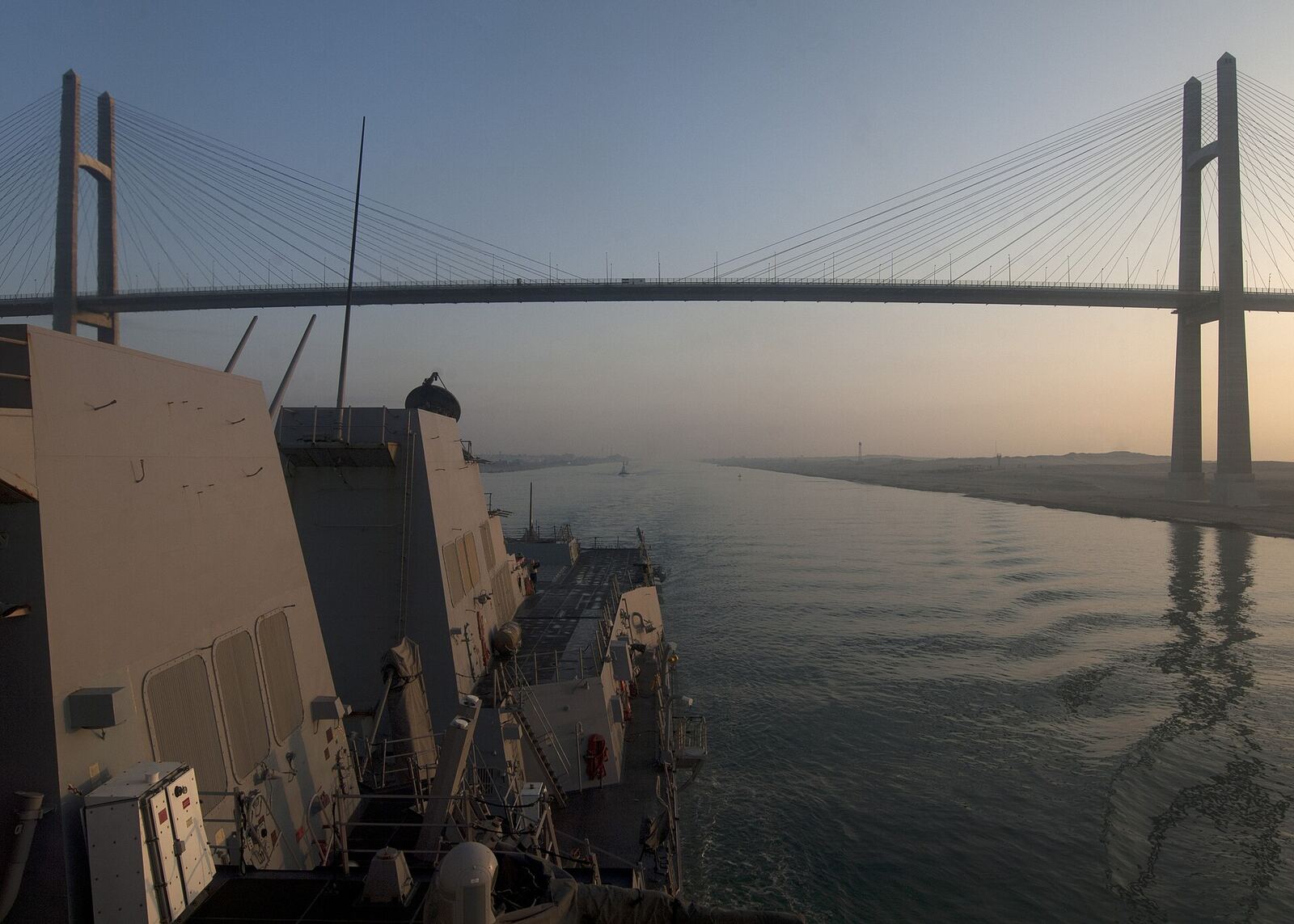 Naval Ship | Love Hurtz A naval vessel travels beneath the Vasco da Gama Bridge in Lisbon, Portugal, illustrating themes of journeys and transitions.