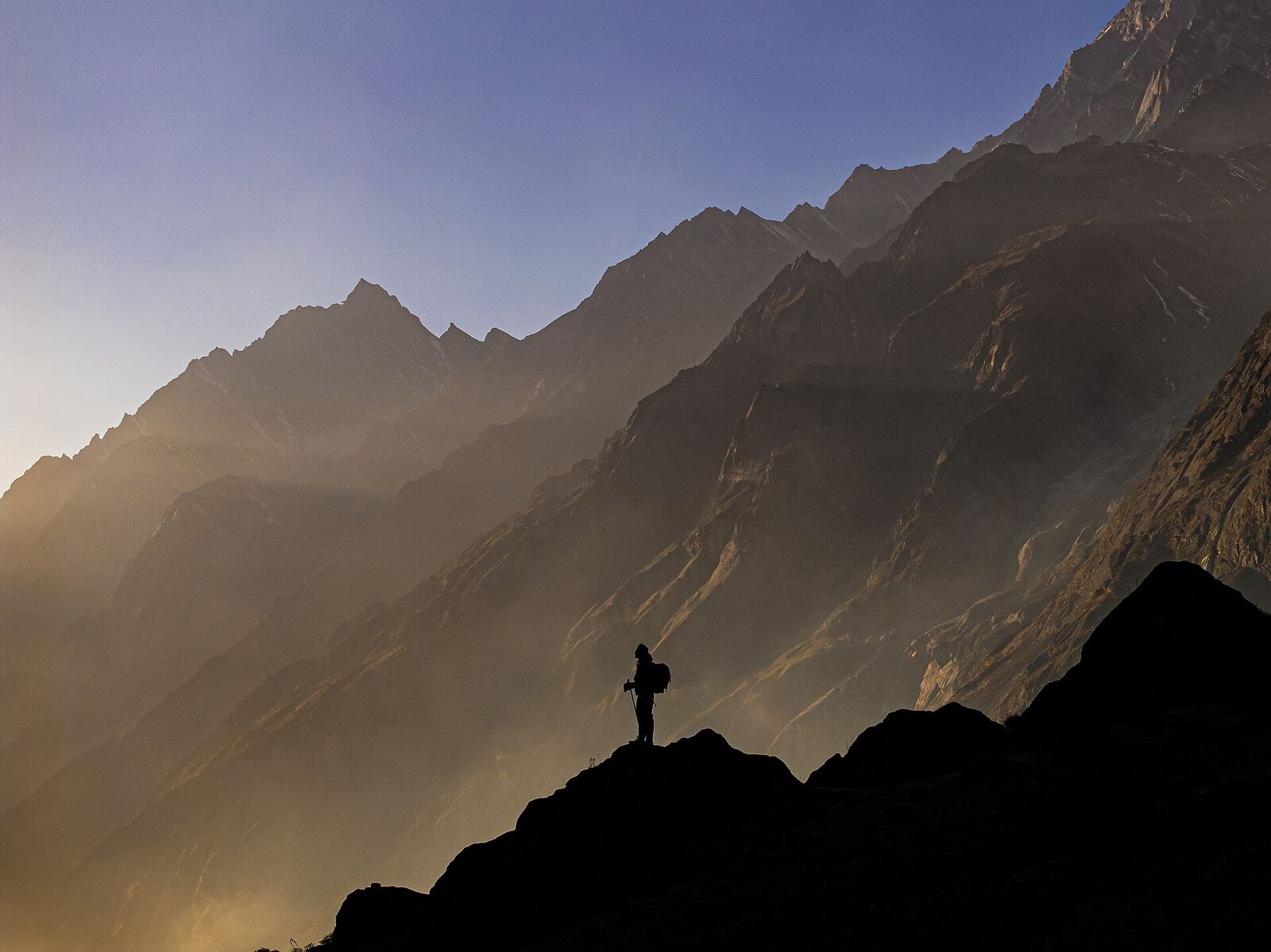 A silhouetted hiker stands atop a rocky outcrop overlooking vast mountains, finding solace in nature during betrayal.
