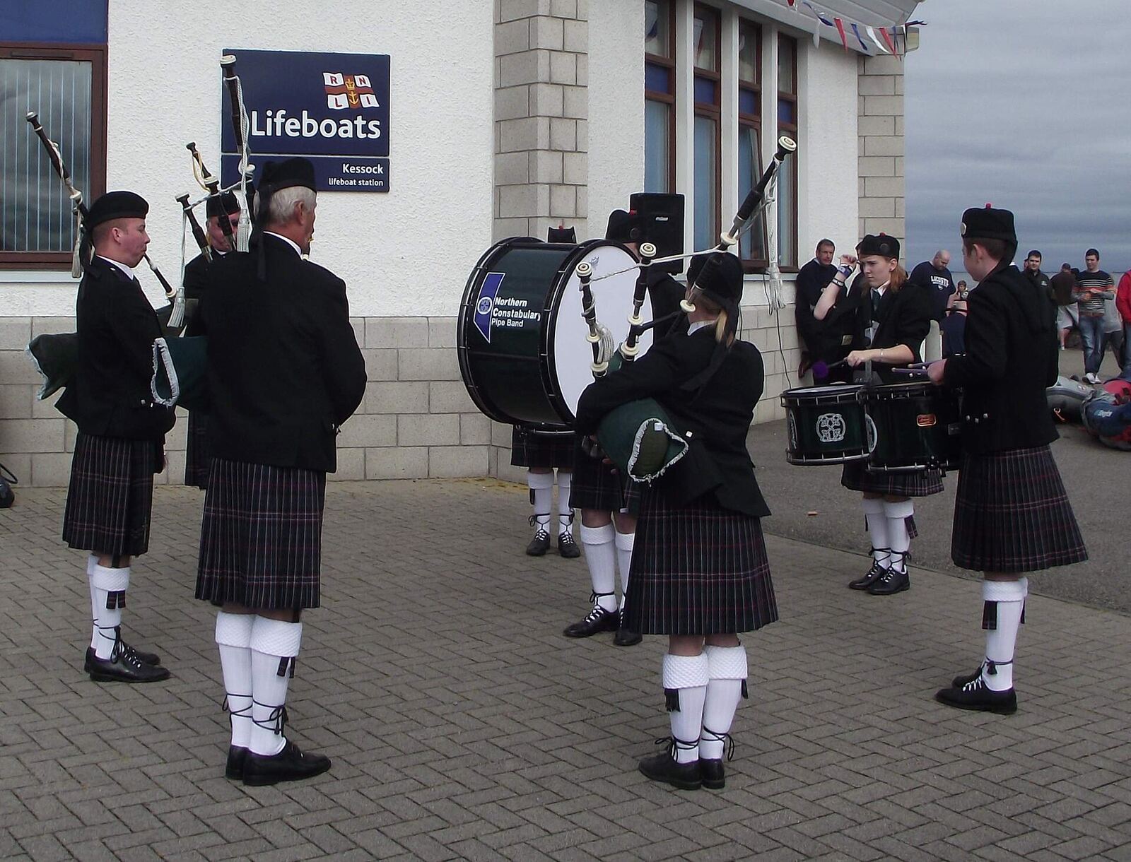 Scottish Pipe Band | Love Hurtz A Scottish pipe band performs near a lifeboat station, capturing a moment of cultural expression and grief support.