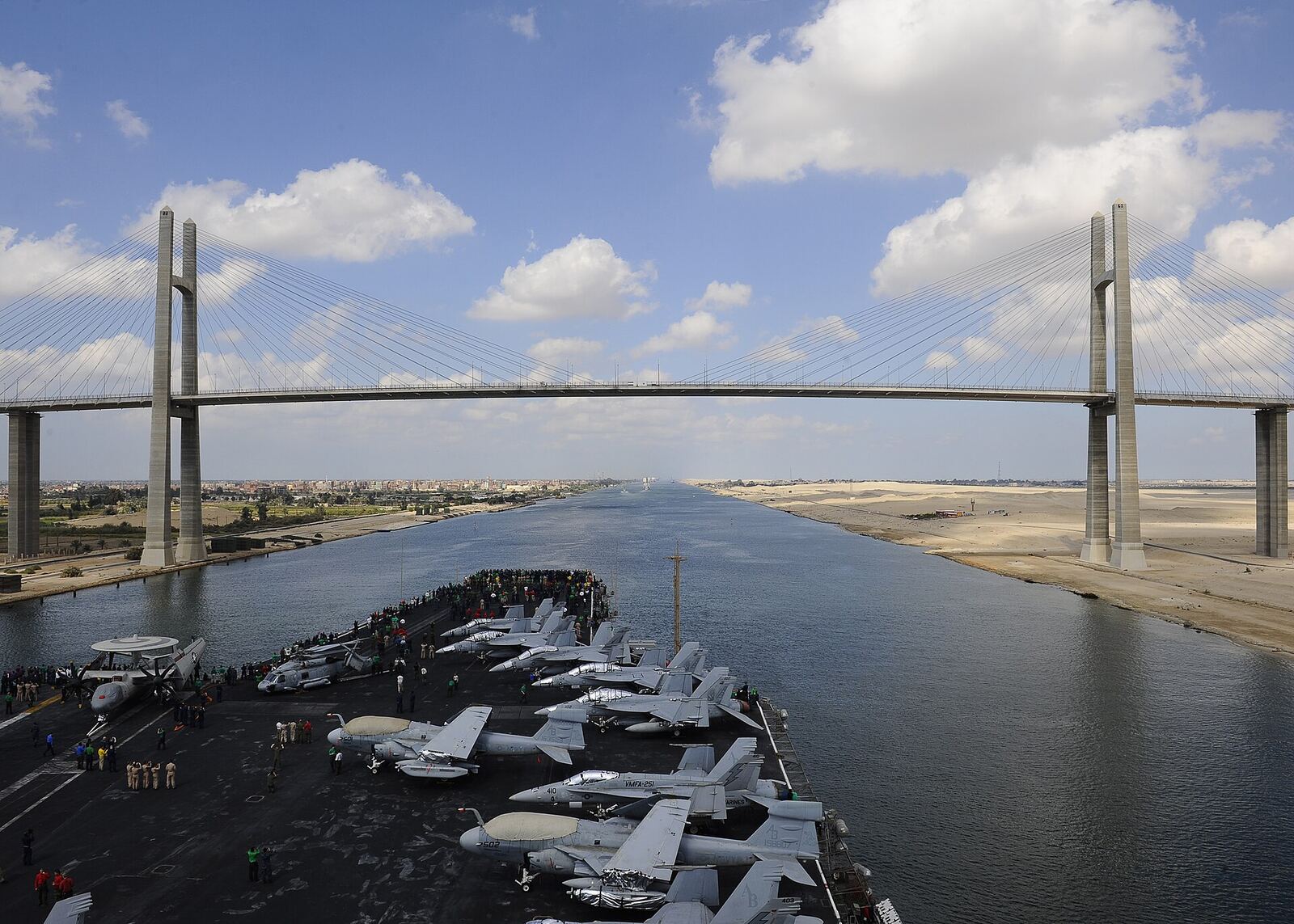Suez Canal | Love Hurtz A U.S. Navy aircraft carrier travels through the Suez Canal under a cable-stayed bridge.