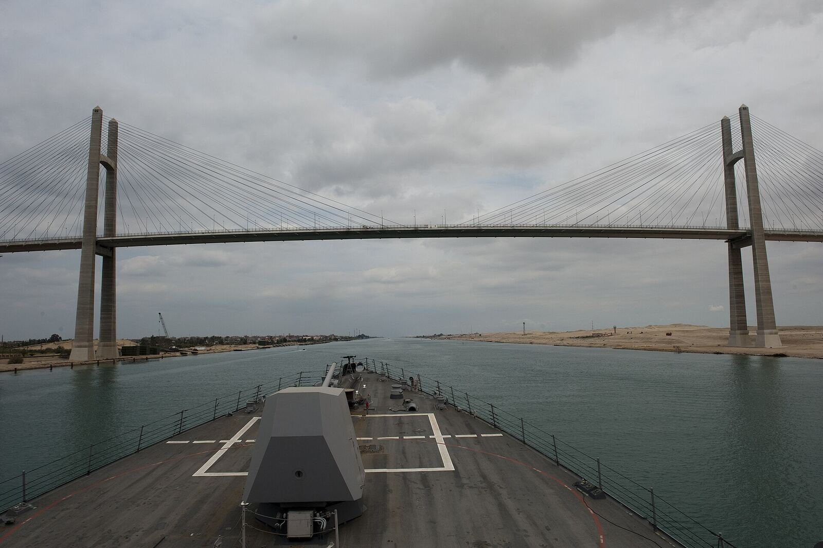 Suez Canal Ship | Love Hurtz A naval vessel travels through the Suez Canal under a cable-stayed bridge, representing journeys through difficult.